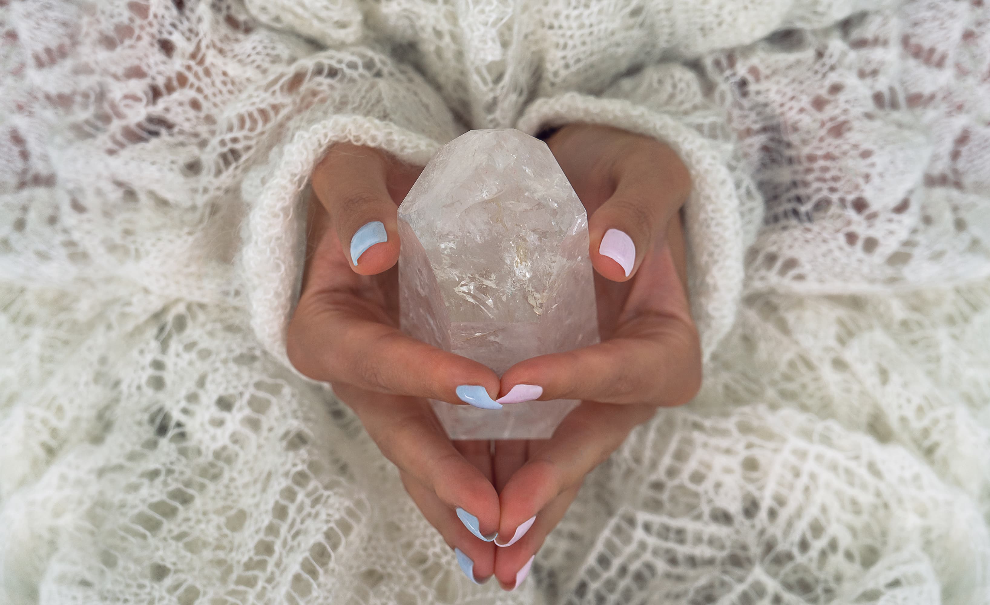 Two hands cradling a clear quartz crystal against a soft knit shawl