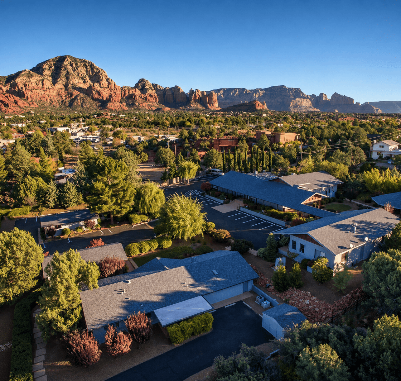 Aerial view of the Sedonya retreat campus and lodging buildings nestled among trees, with Sedona's red rock mountains rising behind
