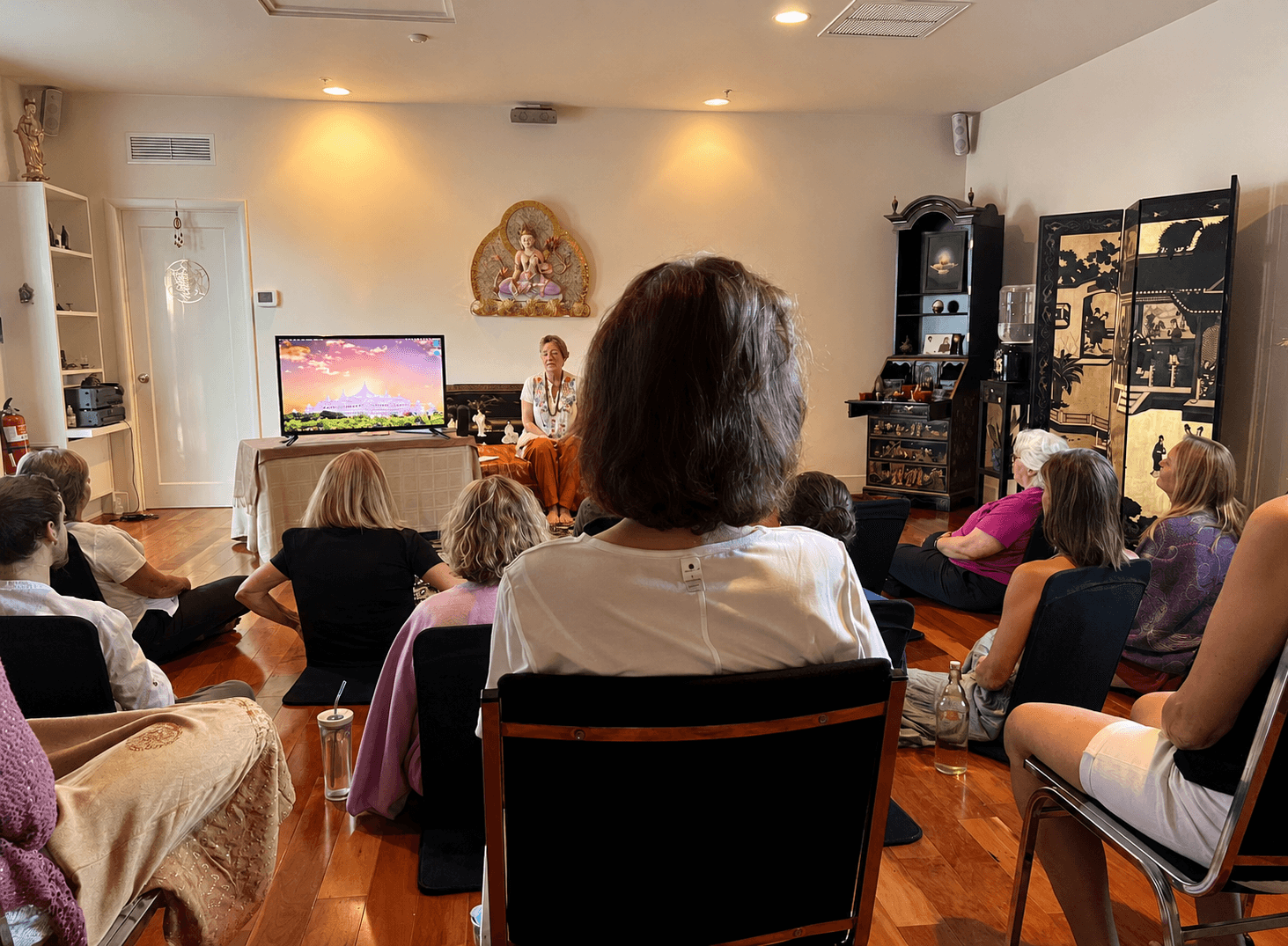 A meditation class gathered on cushions and chairs in Guan Yin, facing a teacher seated before an altar to the Bodhisattva of Compassion