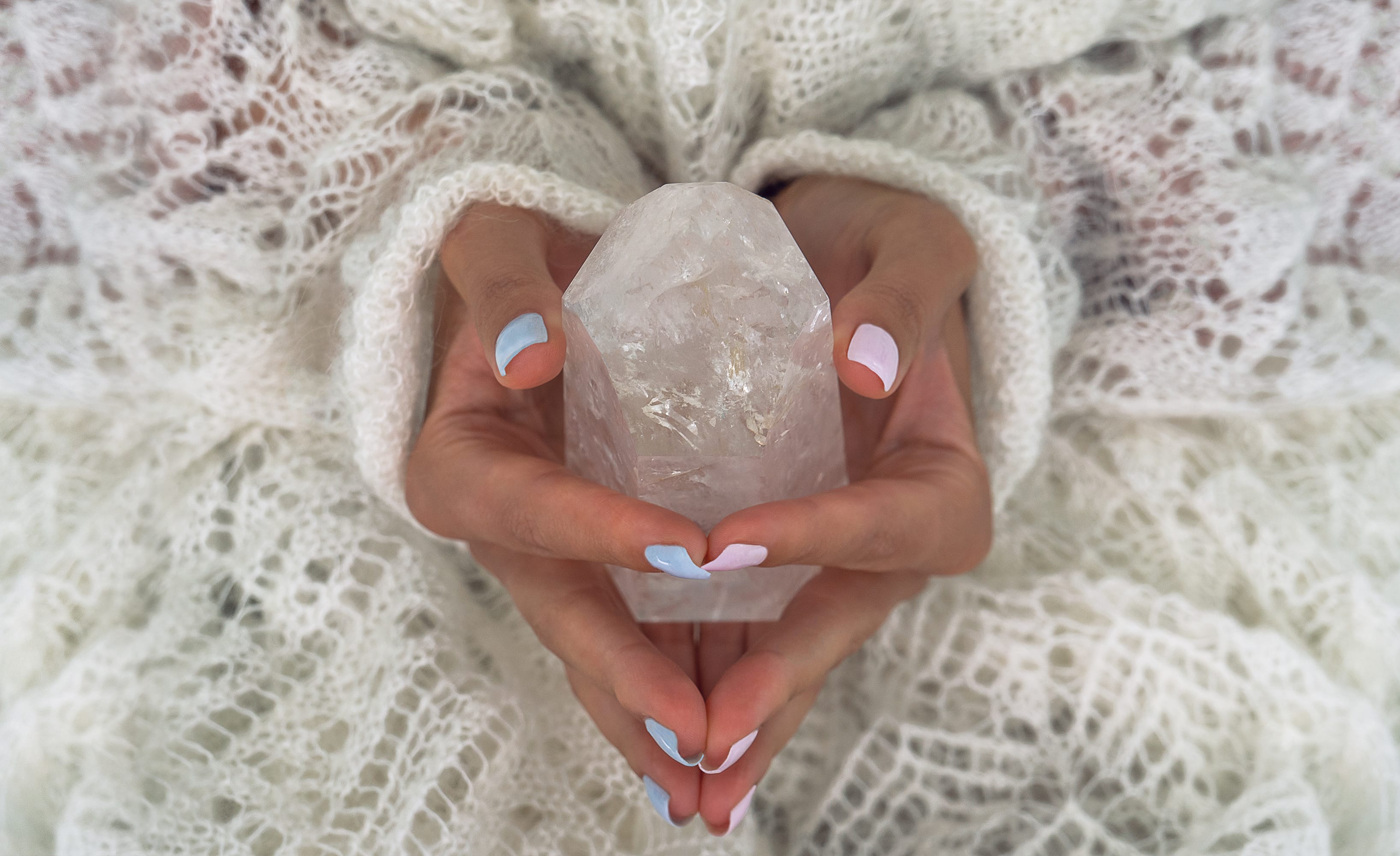 Two hands cradling a clear quartz crystal against a soft knit shawl