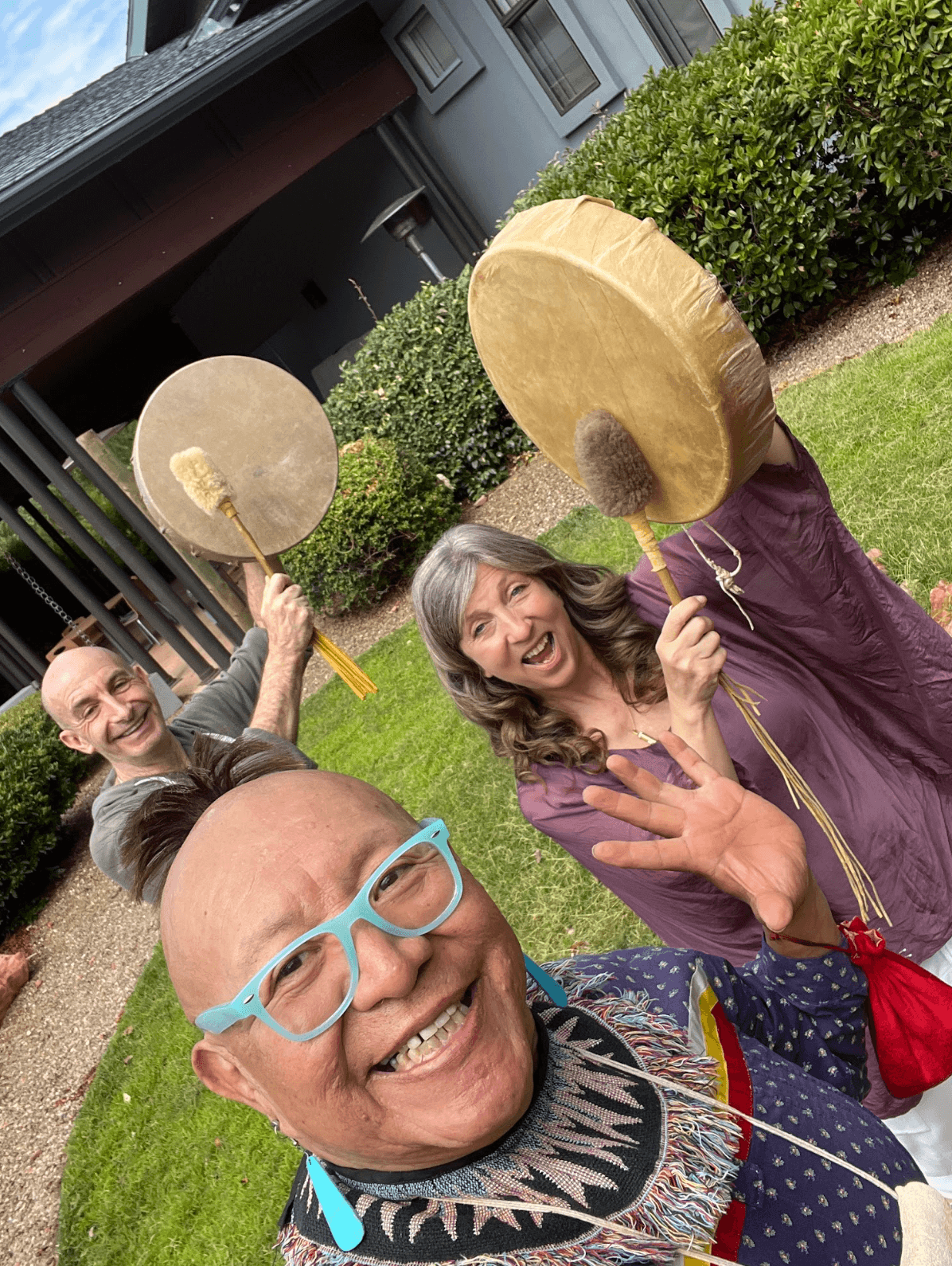 Three retreat guests laughing together, hand drums raised, moments before a movement session