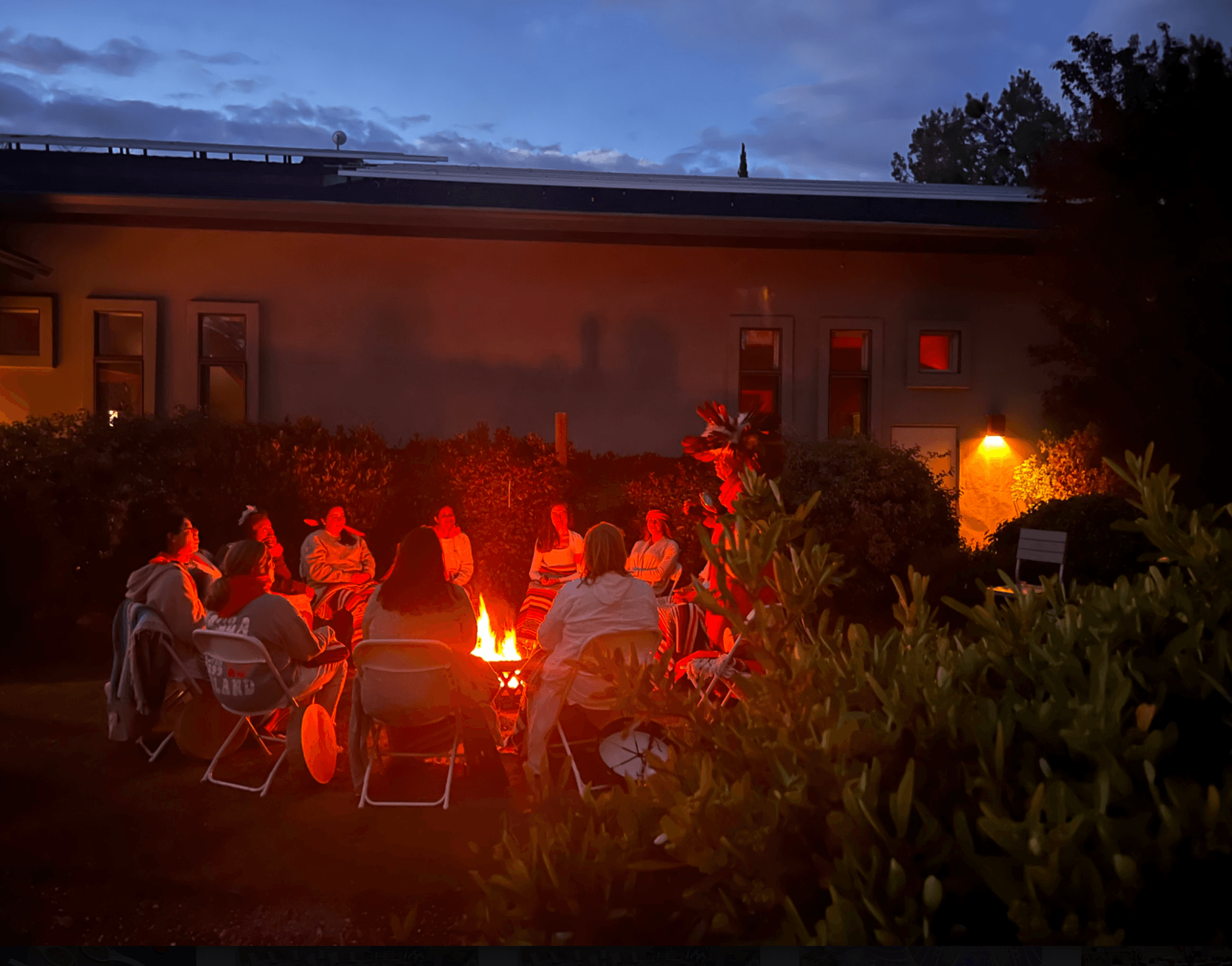 A retreat group gathered in a circle around a fire at dusk during a closing ceremony