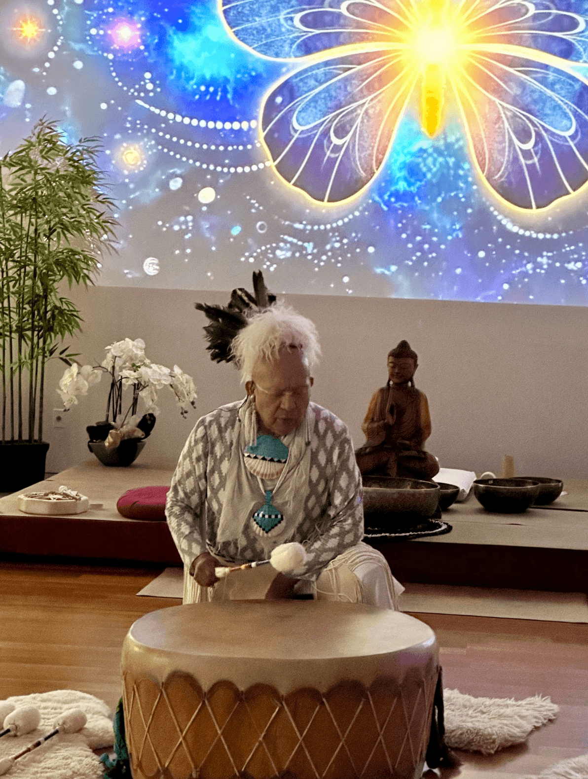 A sound healer playing a large hand drum inside the Cathedral, singing bowls and a Buddha statue nearby