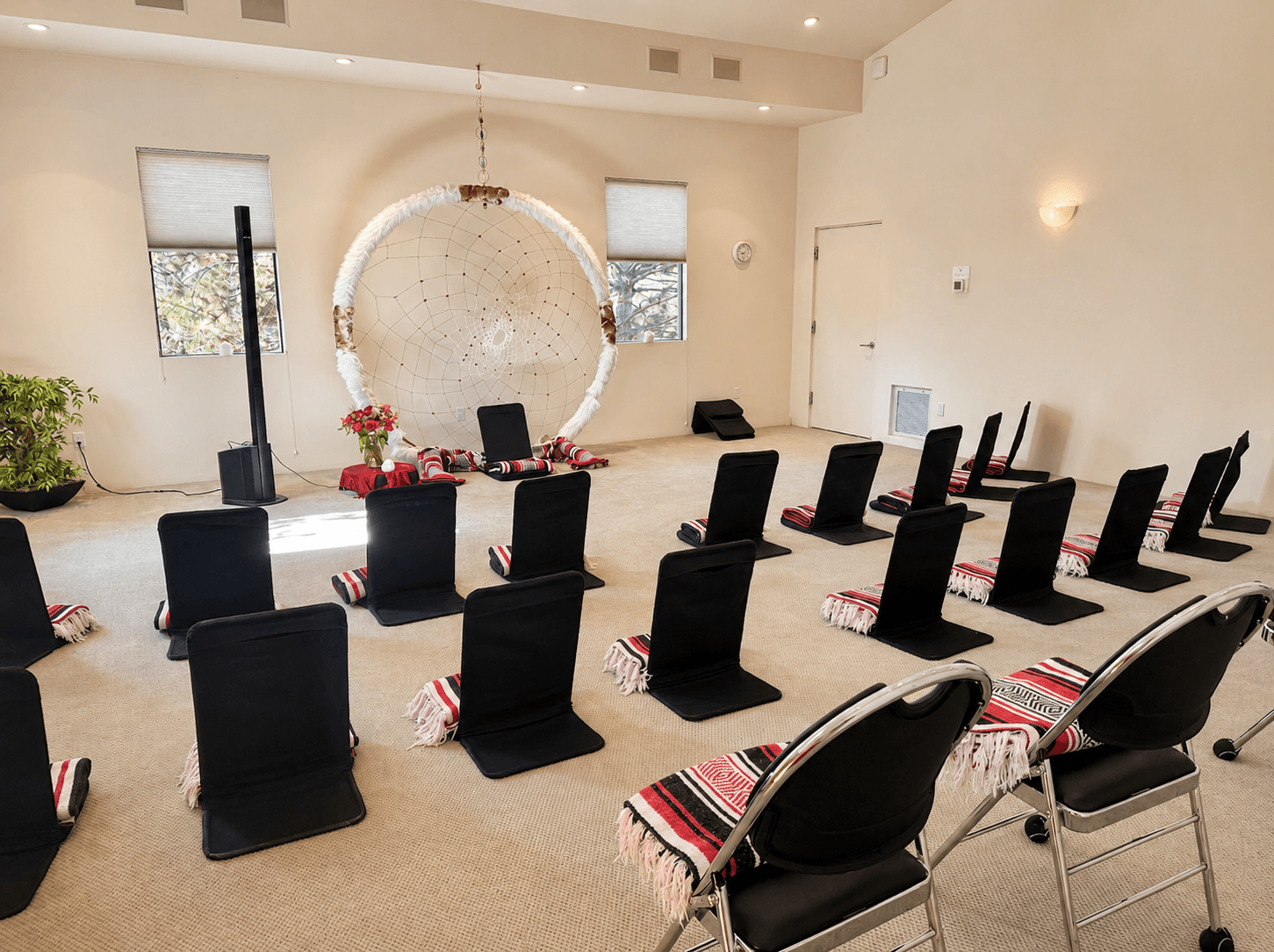 Rows of black backjack meditation chairs facing forward toward a dreamcatcher altar, set up retreat-style inside Sicatuva