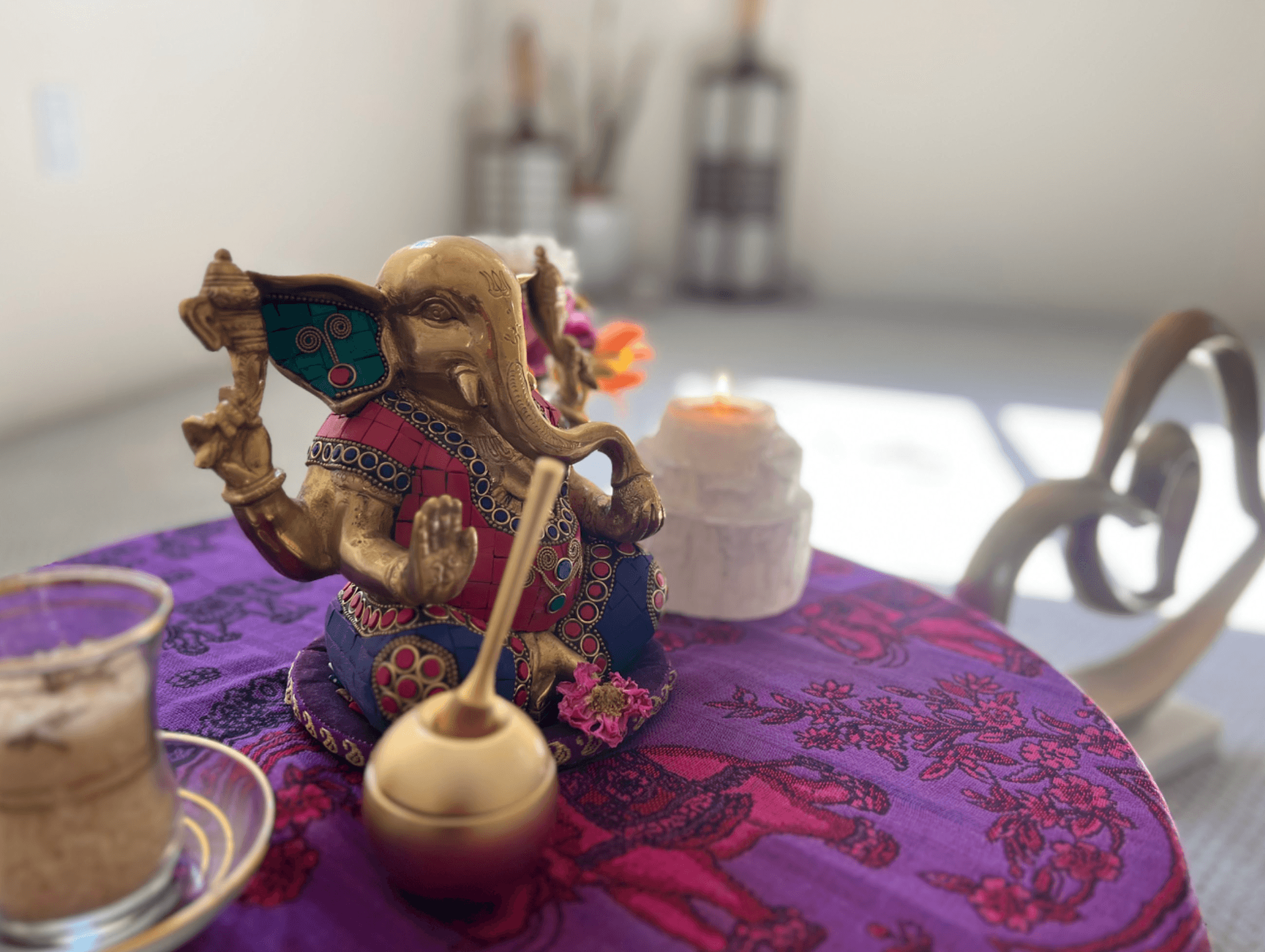 A brass Ganesh statue on the room's small altar, with chai and incense beside a purple tablecloth and candlelight