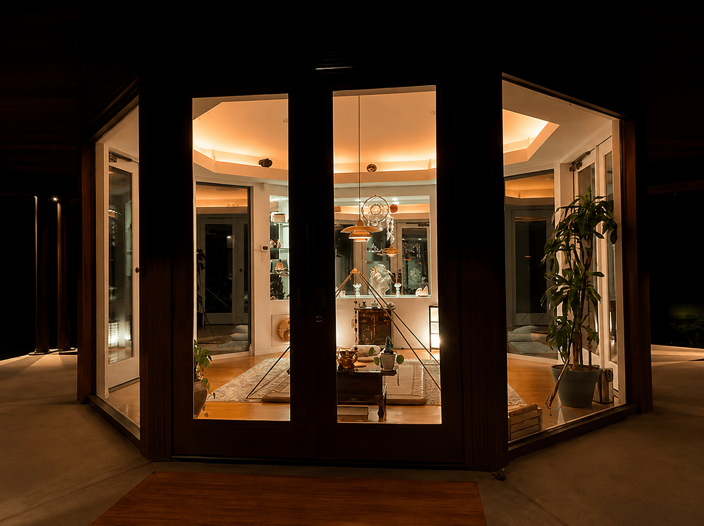 The Temple's glass walls glowing from within at night, warm light spilling out from the octagonal room onto the dark porch