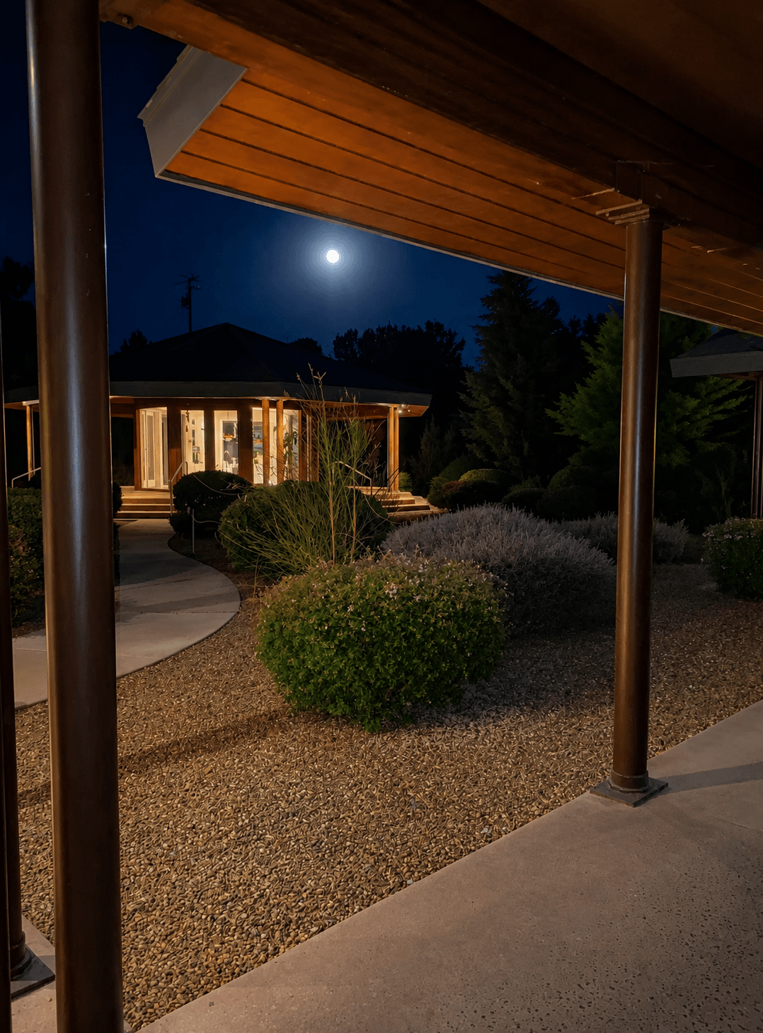 Wooden pillars frame the path home — the Temple glowing at the end of it, a moon rising over the roofline