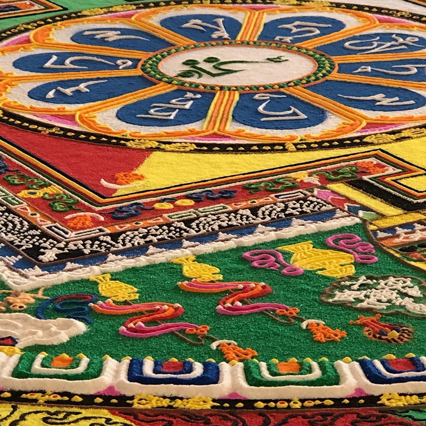 A close view of a sand mandala mid-creation — lotus petals of colored sand encircling sacred script, built one grain at a time before it's swept away