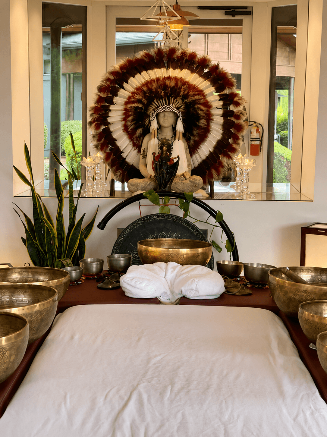 A seated figure, feathered and still, keeps watch over the bowls and the table below